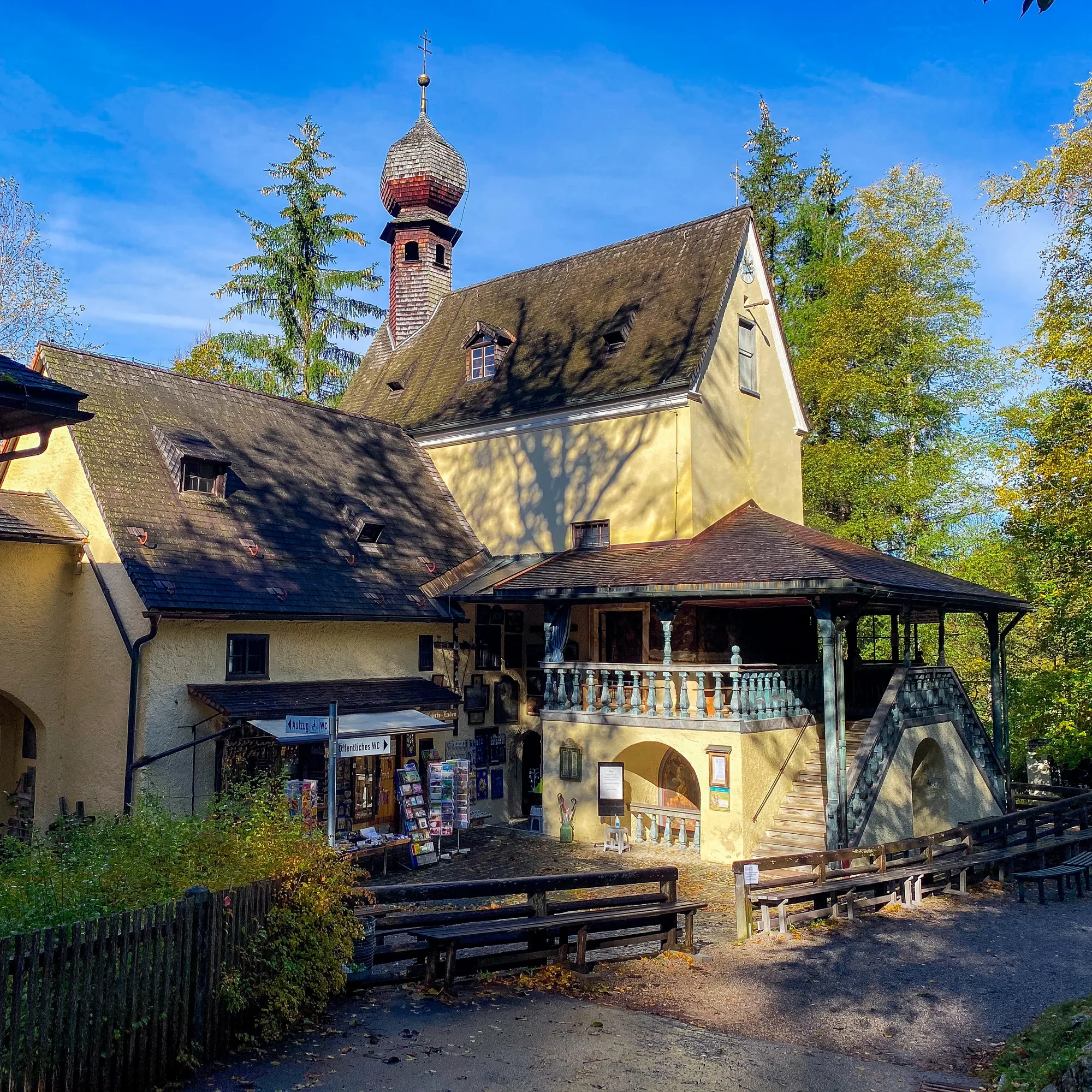 Gelbes Haus mit Zwiebelturm und Holzbalkon vor blauem Himmel