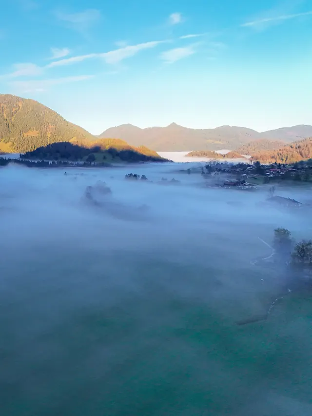 Dorf am See im Morgennebel, umgeben von Bergen