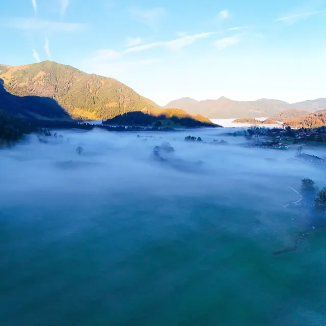 Ground fog over a lake in front of forested mountain slopes