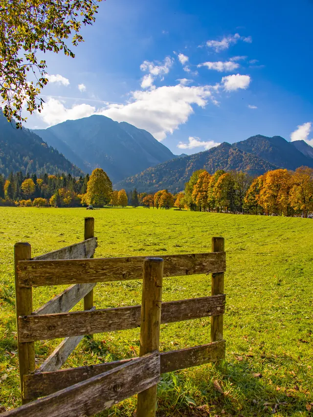 Holzzaun vor grüner Weide mit Bergkette im Hintergrund