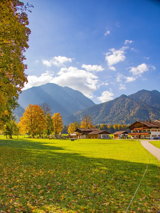 Autumn-colored trees against mountains, houses at the edge of a meadow